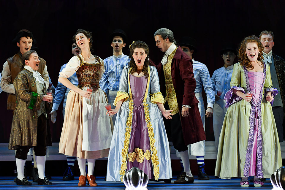 A group of students, dressed in historical costume, performing in an opera on stage.